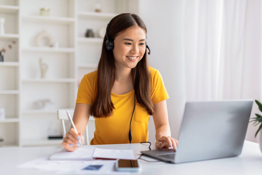 joyful young woman wearing headset multitasking writing